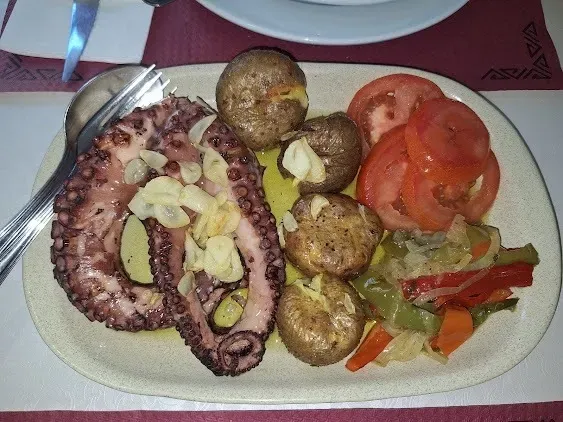 Tentáculos de pulpo, patatas asadas, tomates y verduras en un plato blanco.