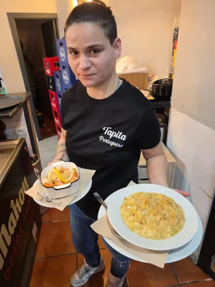 Persona con camisa negra sosteniendo dos platos de comida en el interior de un edificio.