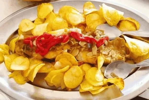 Plato de comida con patatas fritas y salsa roja sobre la carne en una fuente blanca.
