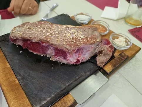 Gran filete crudo sobre una piedra caliente con salsas en una mesa.