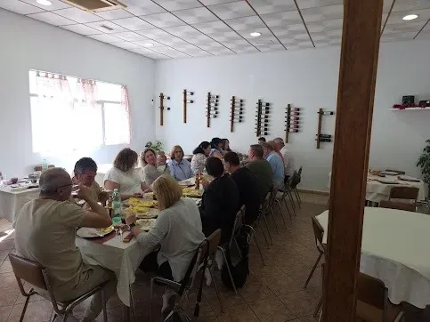Personas sentadas en una mesa larga en una habitación luminosa, compartiendo una comida o reuniéndose.