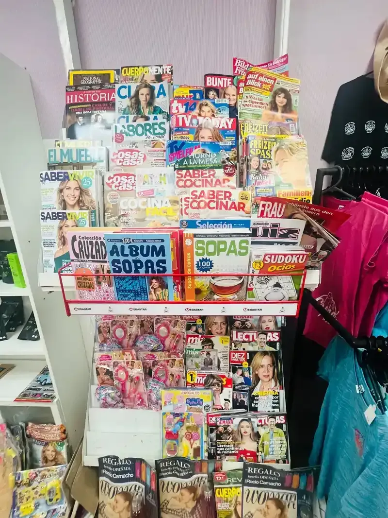 Un estante metálico lleno de diversas revistas y libros de crucigramas dentro de una tienda.