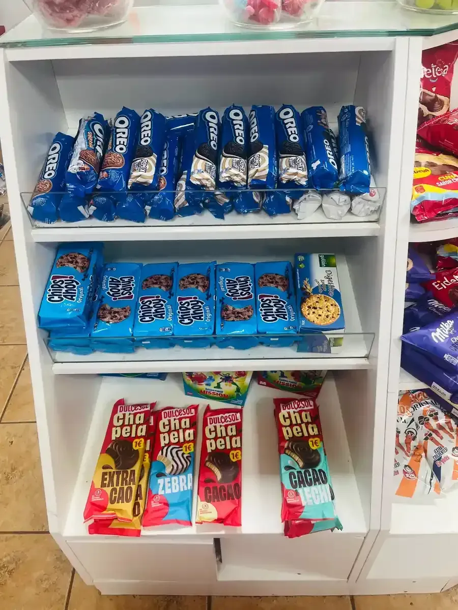 Estanterías blancas en una tienda repletas de filas de paquetes azules de galletas Oreo y varias barritas de chocolate.