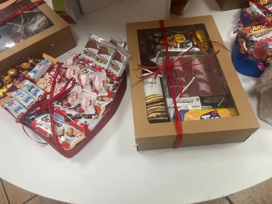 Sobre una mesa blanca, reposan cestas de regalo repletas de diversos aperitivos y dulces, incluyendo chocolates y caramelos.