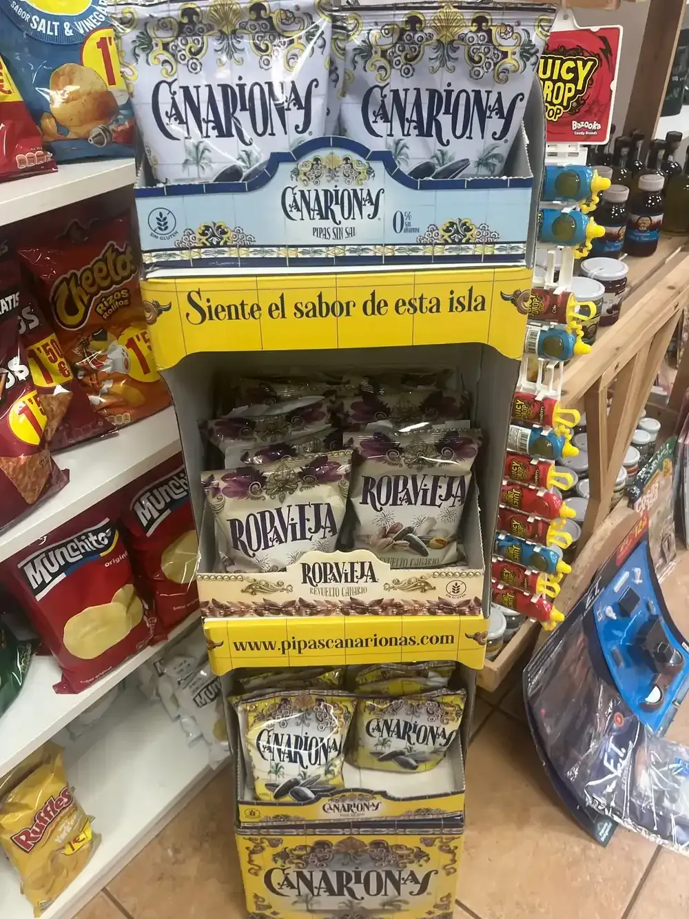 Un expositor en la tienda con bolsas de snacks de la marca Canarionas, con envases y diseños en amarillo y blanco.