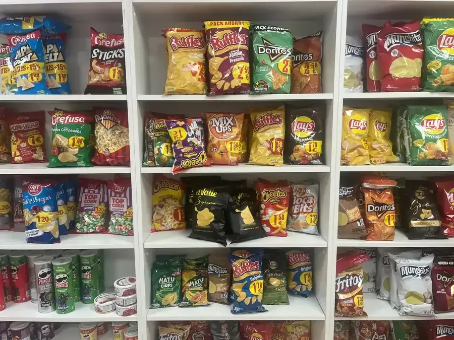 En una tienda, se ven estantes repletos de una variedad de coloridas bolsas y botes de aperitivos.