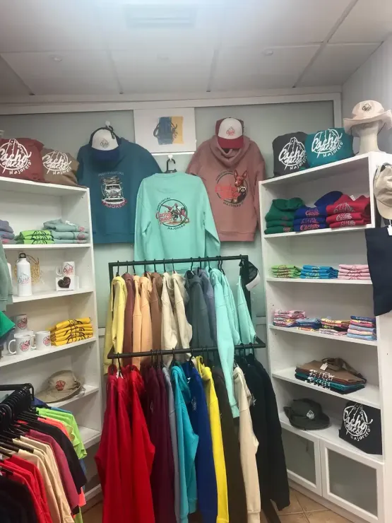 El interior de una boutique de ropa con estantes y un perchero repleto de sudaderas con capucha y gorras de colores.