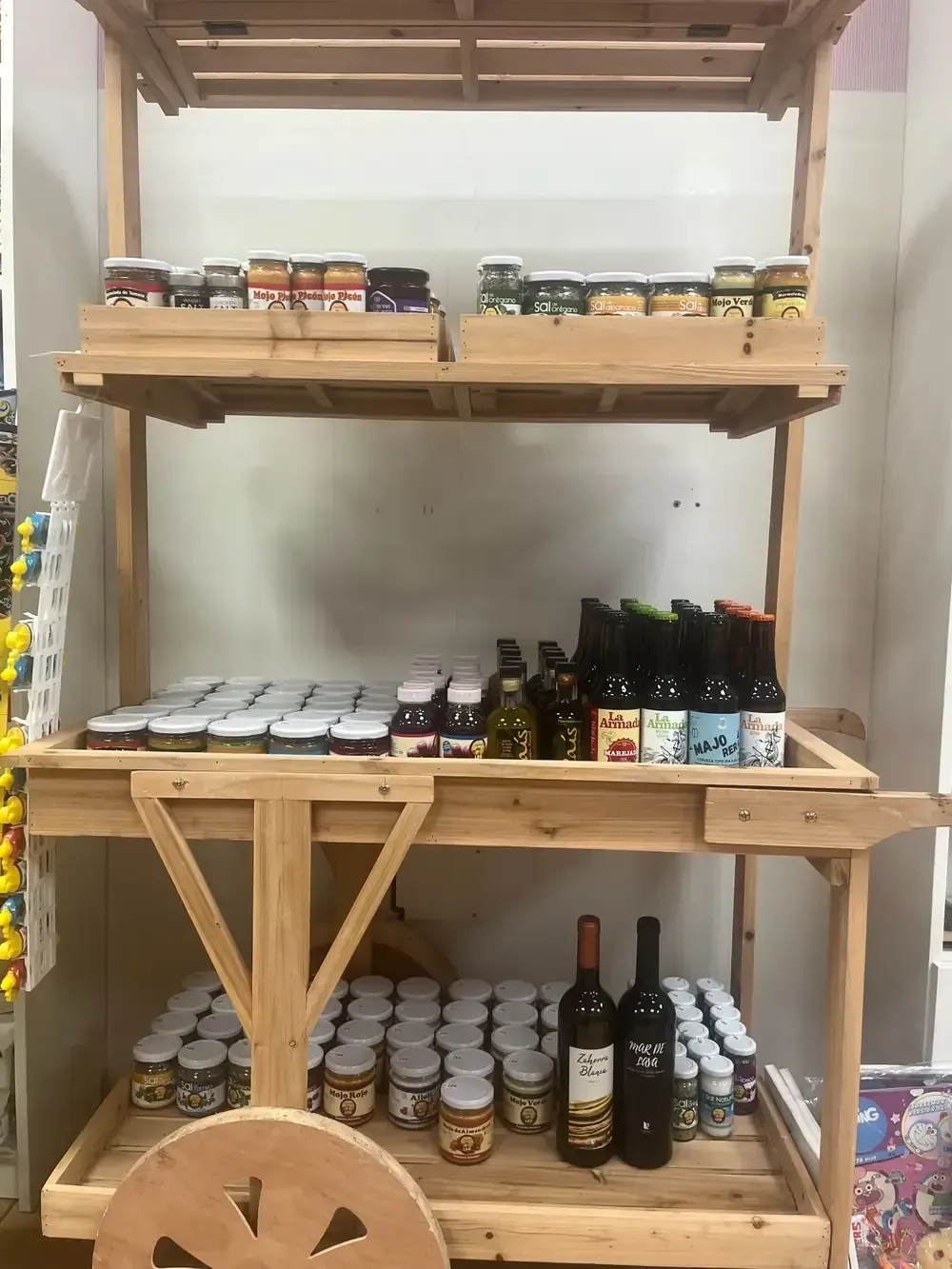 Un carrito de madera escalonado que exhibe varios frascos de conservas, condimentos y botellas de vino.