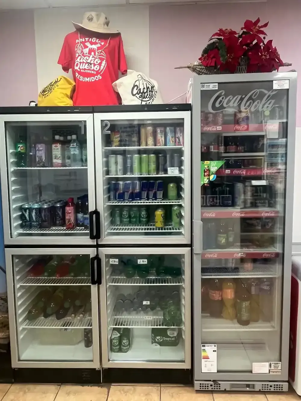 Refrigeradores llenos de bebidas variadas, coronados con una camiseta roja, un sombrero y flores rojas artificiales.