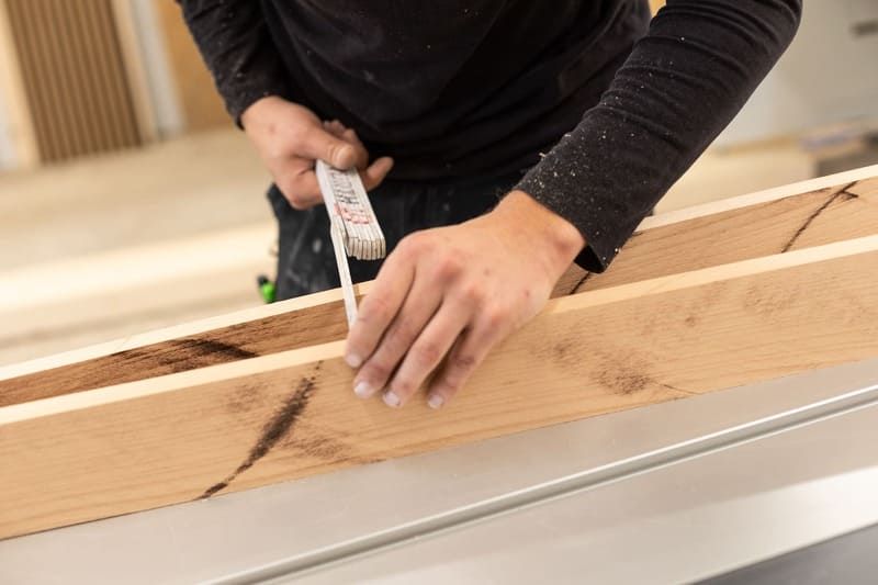 Eine Person misst ein Stück Holz mit einem Maßband.