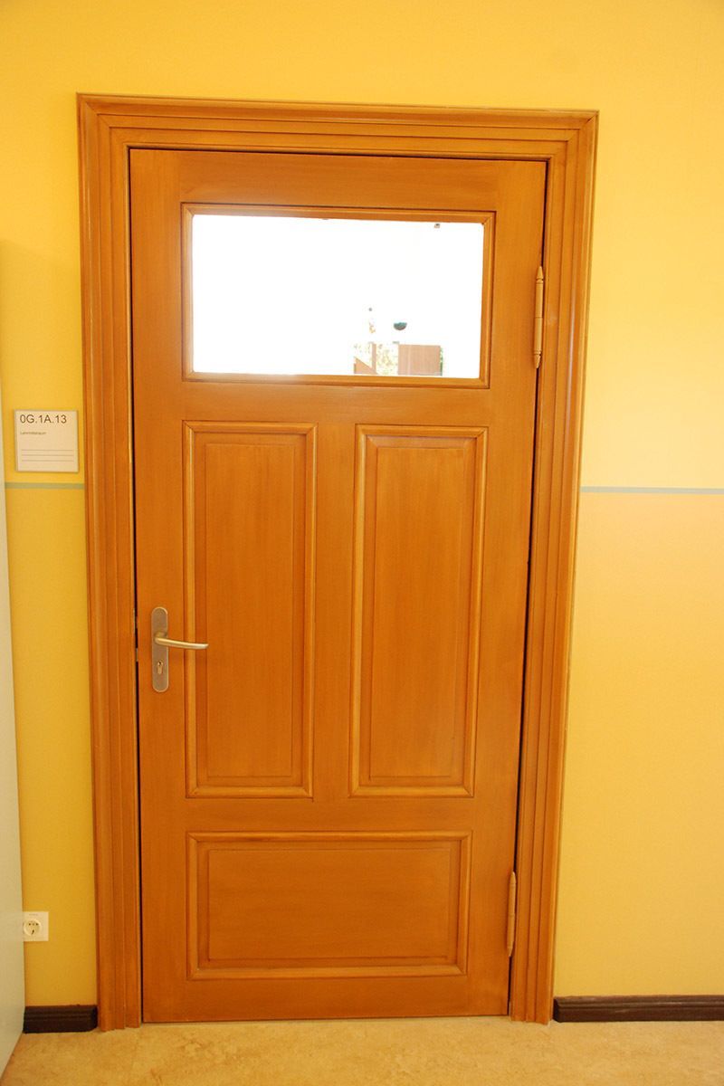 Eine Holztür mit einem kleinen Fenster in einem Raum mit gelben Wänden.