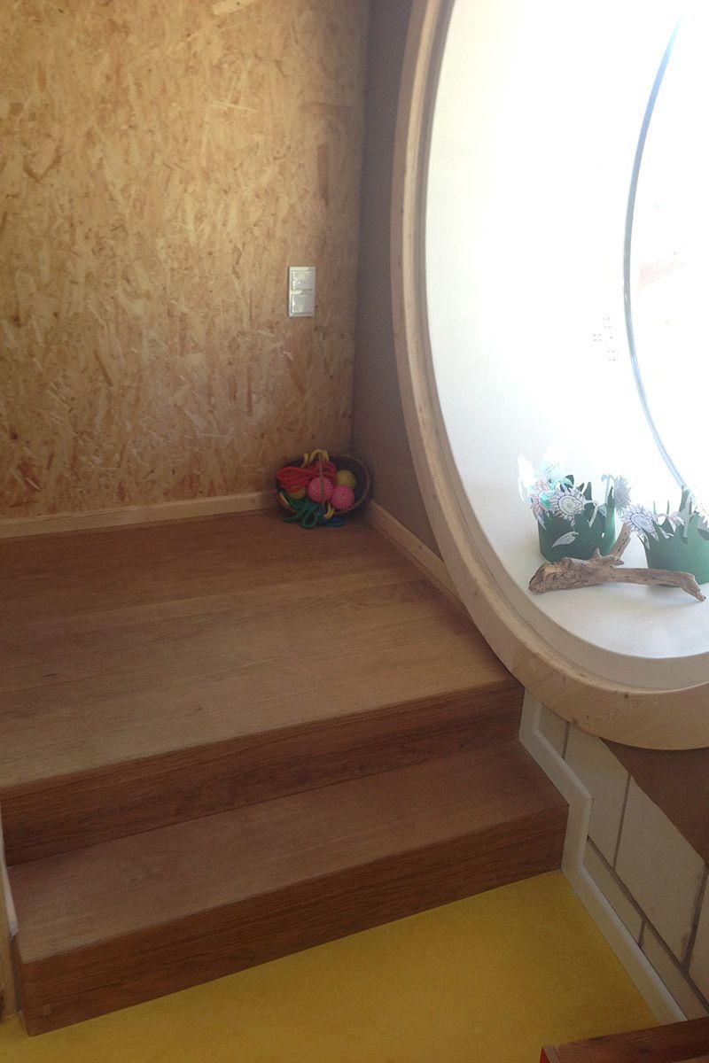 Eine Holztreppe führt hinauf zu einem runden Fenster in einem Zimmer.