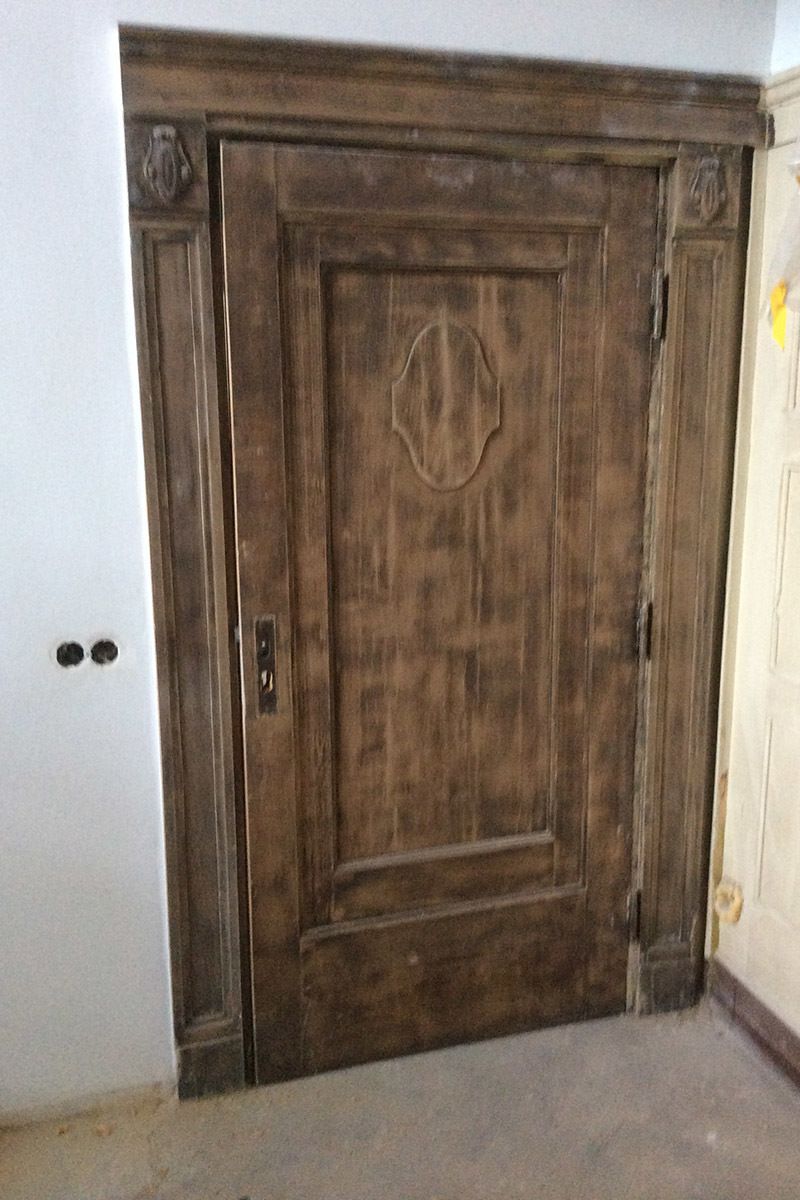 In einem Raum neben einer weißen Wand befindet sich eine große Holztür.