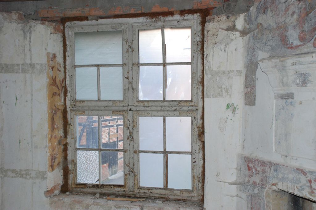 Ein Fenster in einer Backsteinmauer mit der Spiegelung eines Gebäudes darin.