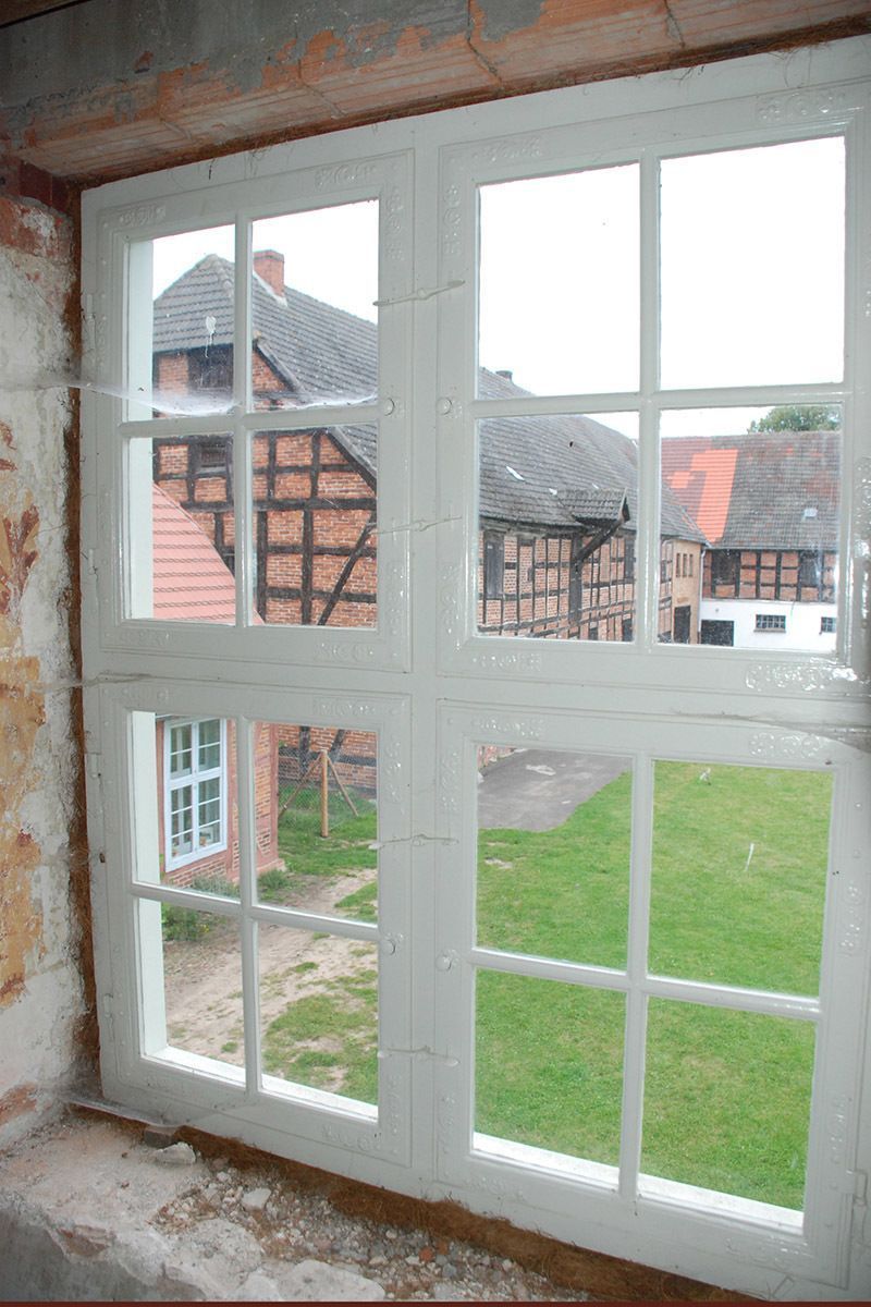Ein Fenster mit Blick auf ein Backsteingebäude und eine üppige grüne Wiese.