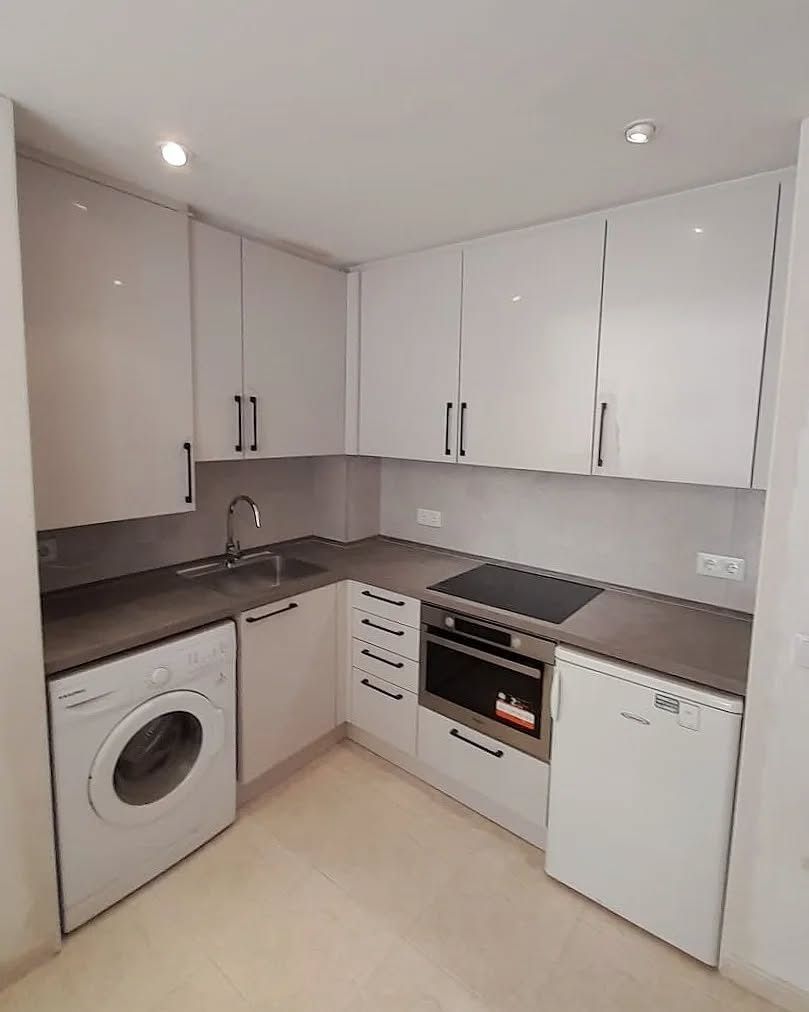 Una cocina con gabinetes blancos, lavadora y secadora, una estufa y un refrigerador.