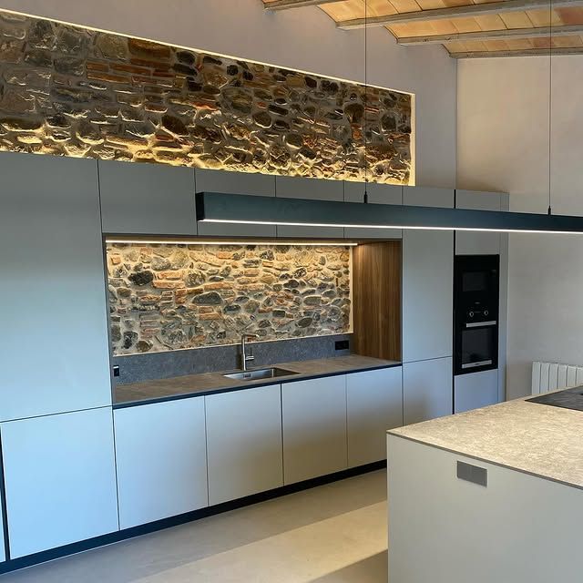 Una cocina con pared de piedra y gabinetes blancos.
