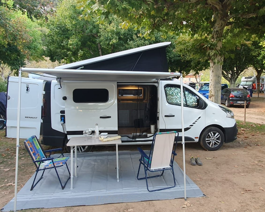 Interior de una furgoneta camper blanca con cocina, asientos y televisión.
