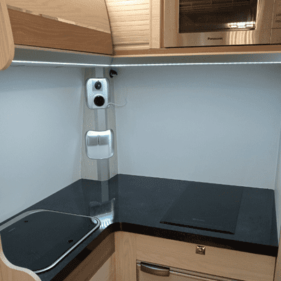 Vista interior de la cocina de una autocaravana con encimera, microondas, placa de cocina y pequeño armario.