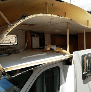 Autocaravana blanca dañada con el techo derrumbado dejando al descubierto el interior, las ventanas y el lado del conductor.