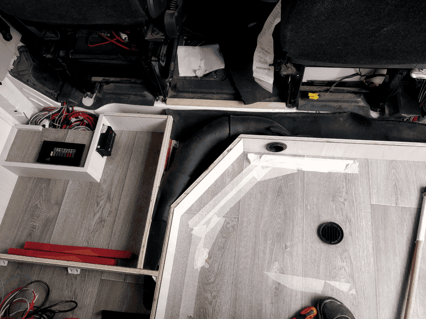 Interior de un vehículo en proceso de renovación; suelo gris, molduras blancas, cableado, conductos de ventilación y asientos parcialmente visibles.