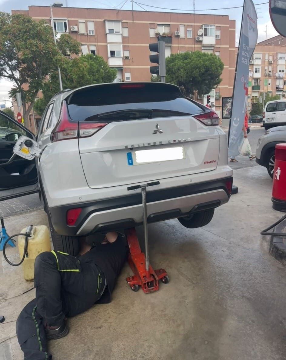 Un hombre está trabajando debajo de un automóvil Mitsubishi blanco.