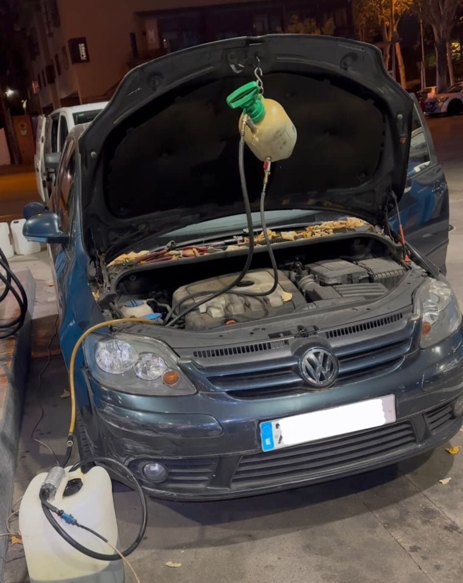 Un Volkswagen azul con el capó abierto está siendo revisado en una gasolinera