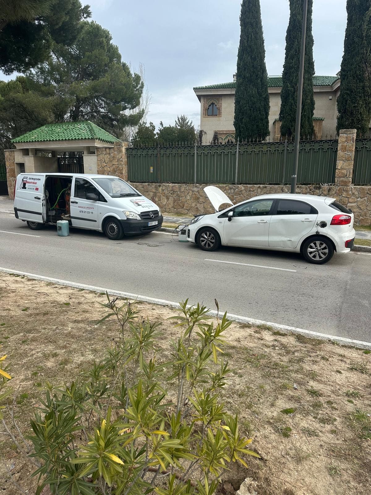 Dos furgonetas blancas están estacionadas al costado de la carretera al lado de un automóvil blanco con el capó levantado.
