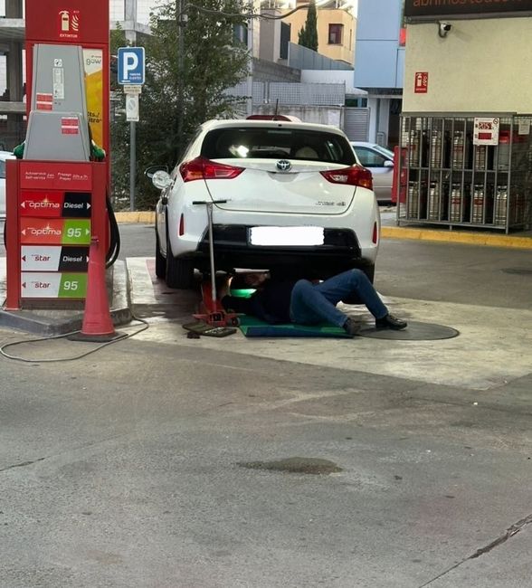 Un hombre está trabajando debajo de un coche en una gasolinera.