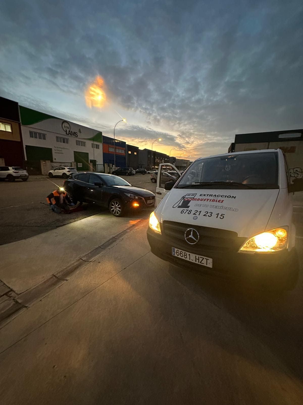 Una camioneta blanca está estacionada al lado de un auto negro en un estacionamiento.