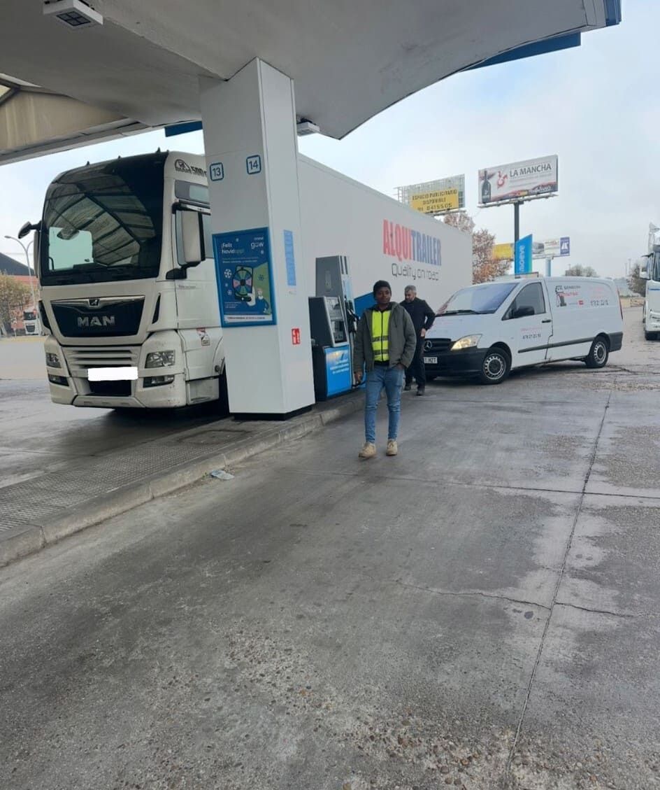 Un hombre está parado frente a un camión en una gasolinera.