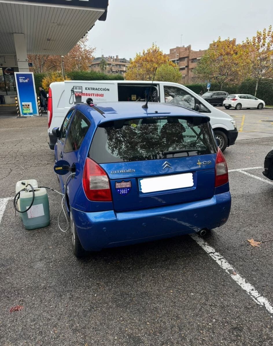 Un coche azul está aparcado en un aparcamiento de una gasolinera.