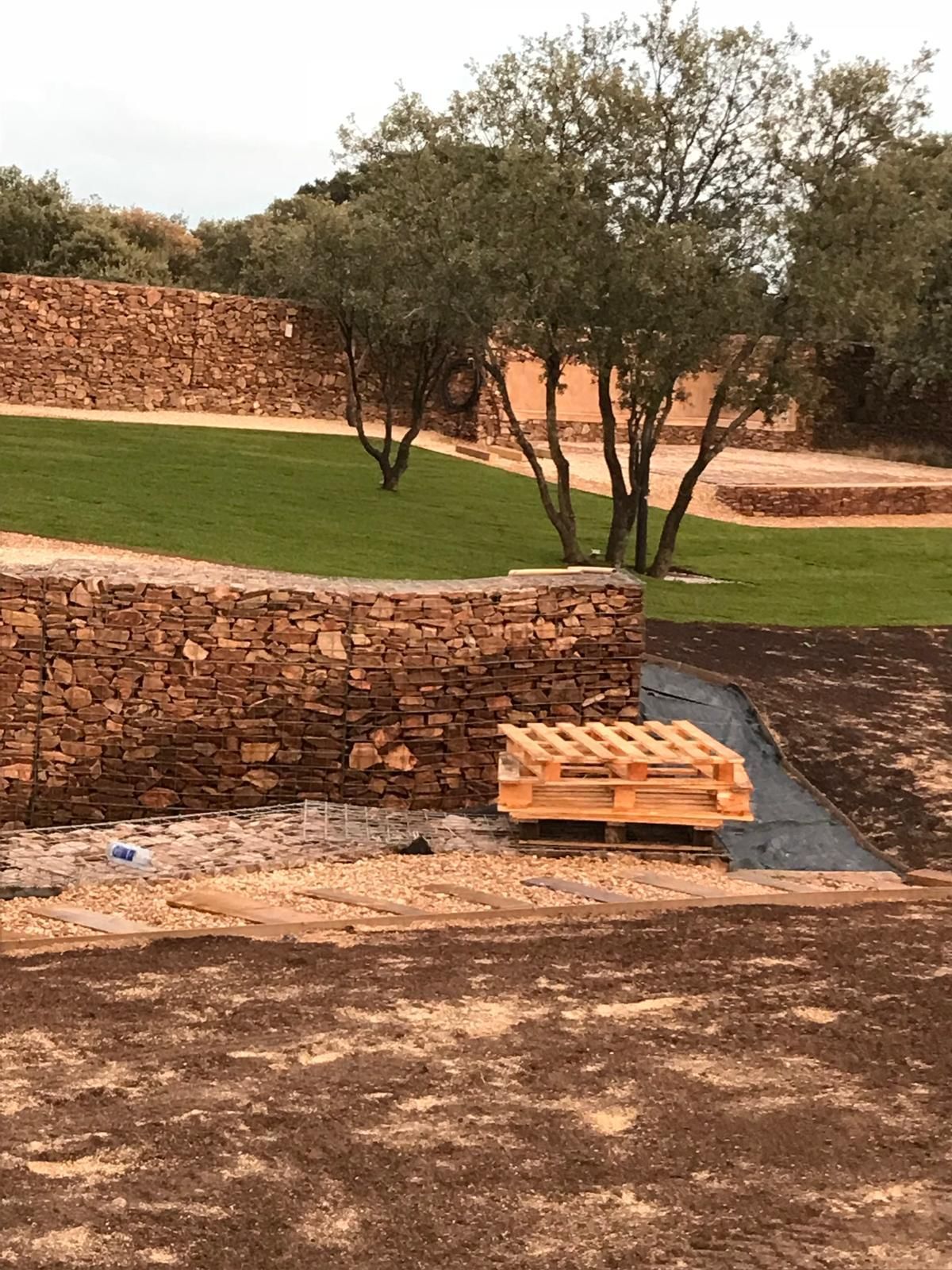 Muros de piedra y paisaje de césped verde con árboles; paleta de madera colocada en el suelo.