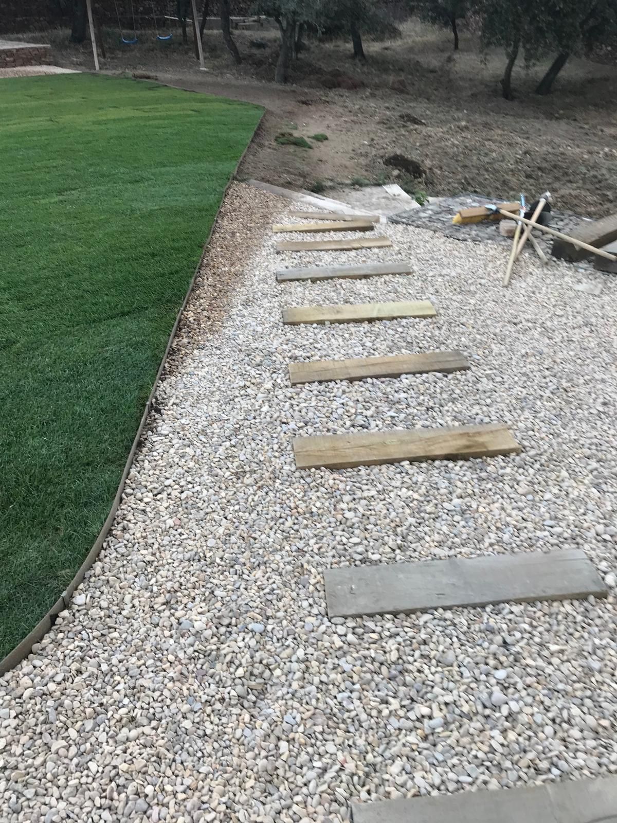 Un camino de grava con tablones de madera forma escalones junto a un césped verde.