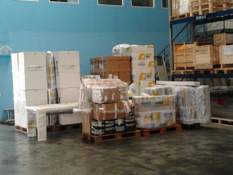 Παλέτες αποθήκης με συσκευασμένα προϊόντα και τυλιγμένες συσκευές στοιβαγμένες σε έναν μπλε τοίχο σε τσιμεντένιο δάπεδο