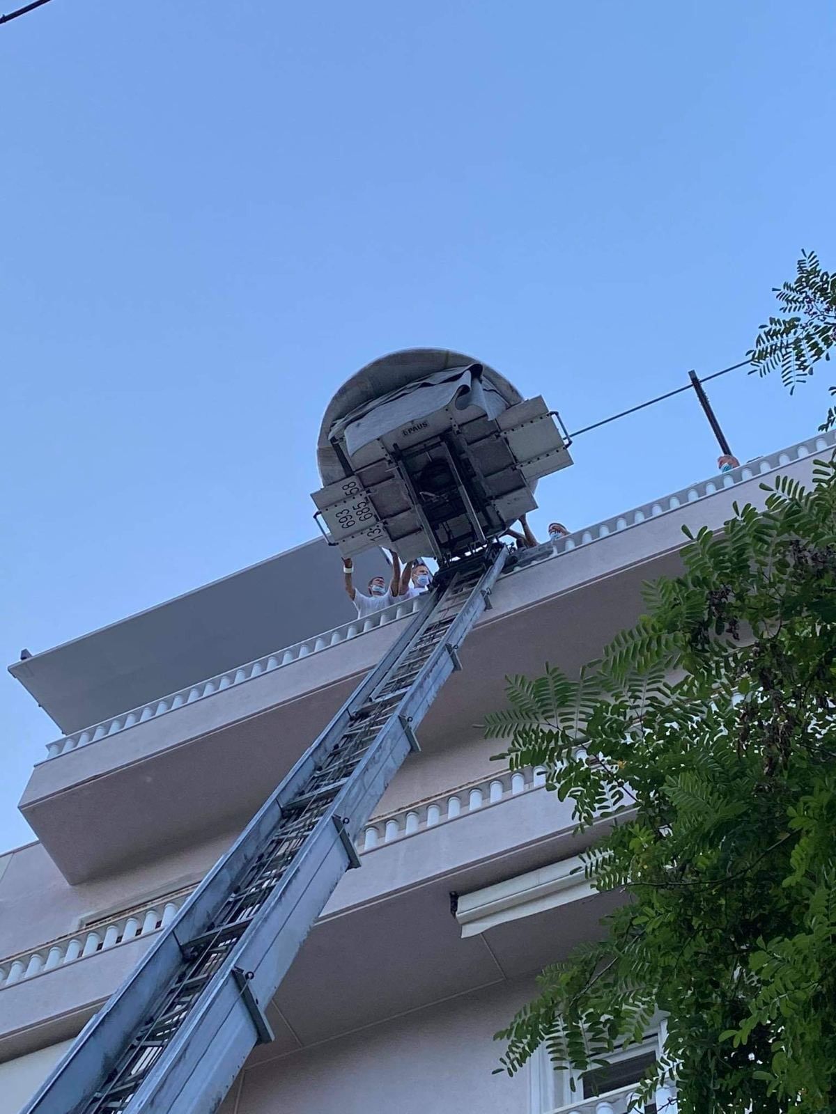 Σκάλα πυροσβεστικού οχήματος που επεκτείνεται σε ένα μπαλκόνι στέγης ενάντια σε έναν μπλε ουρανό