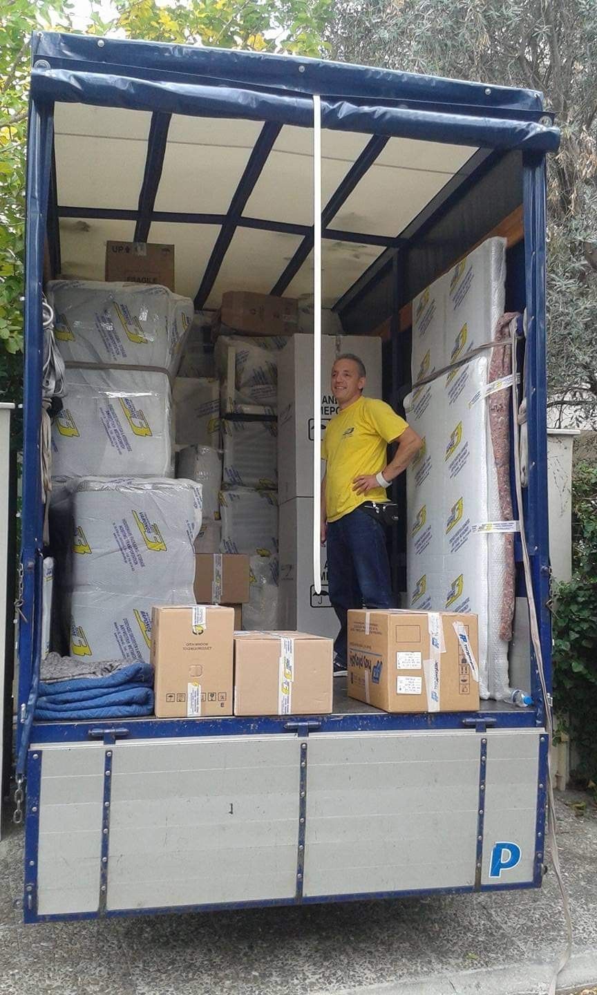 Άτομο που στέκεται σε ένα κινούμενο φορτηγό γεμάτο με τυλιγμένα έπιπλα και κουτιά