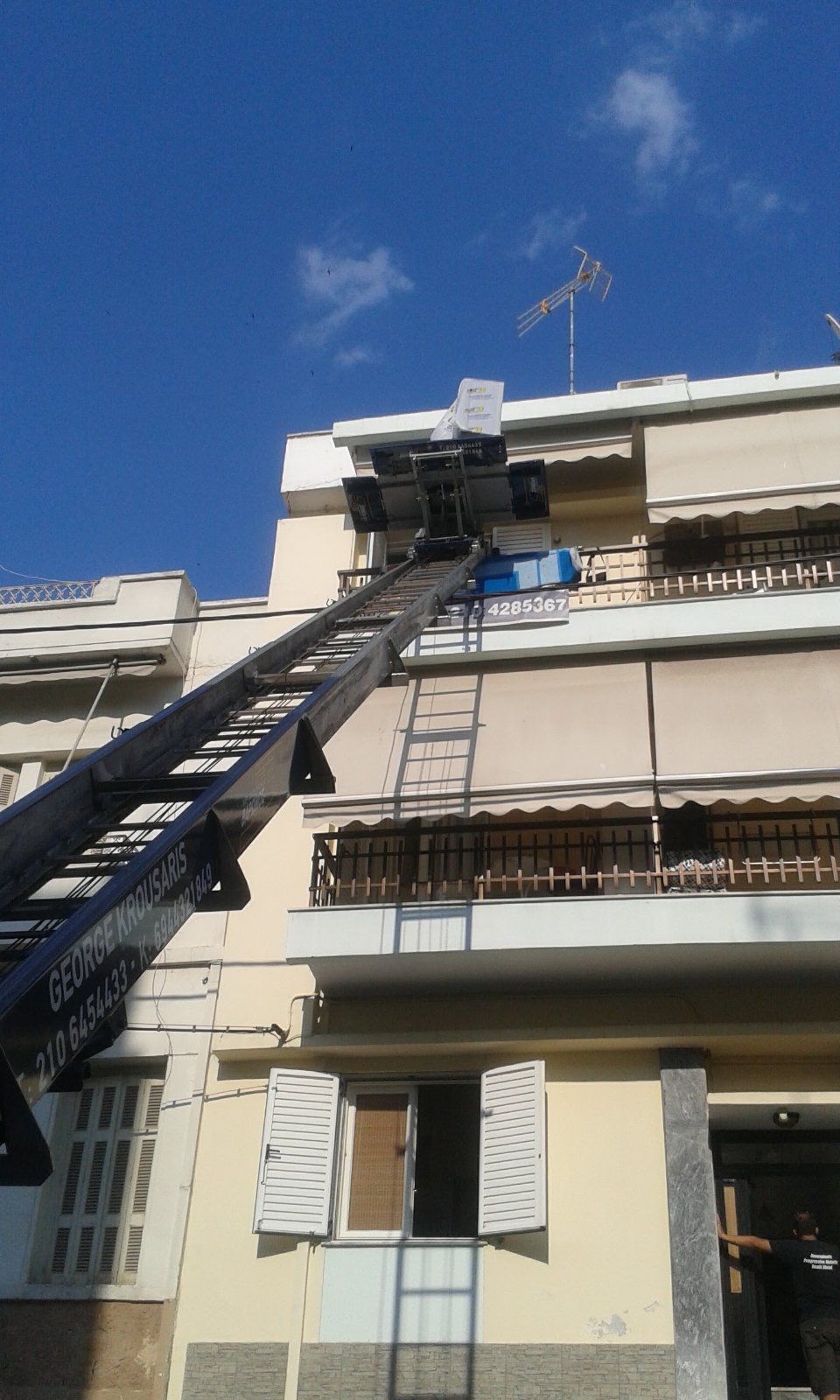 Καλάθι συλλογής κερασιών επεκταμένο σε μια μπεζ πρόσοψη πολυκατοικίας κάτω από έναν γαλάζιο ουρανό