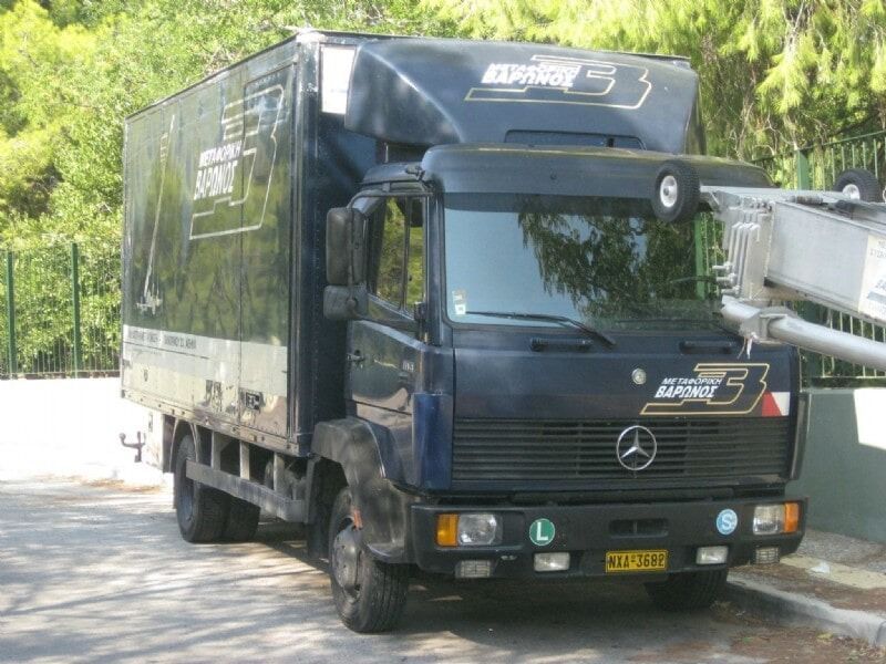 Μπλε φορτηγό παράδοσης Mercedes παρκαρισμένο σε δρόμο δίπλα σε πράσινο