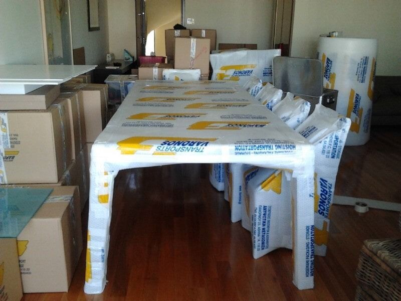Κουτιά από χαρτόνι και ένα τραπέζι καλυμμένο με ένα λευκό πλαστικό φύλλο σε ένα δωμάτιο με ξύλινα πατώματα