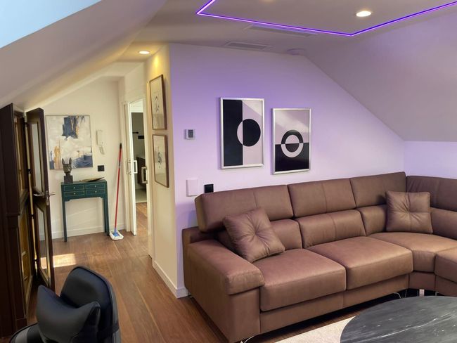 Una sala de estar con un sofá marrón y luces violetas en el techo.