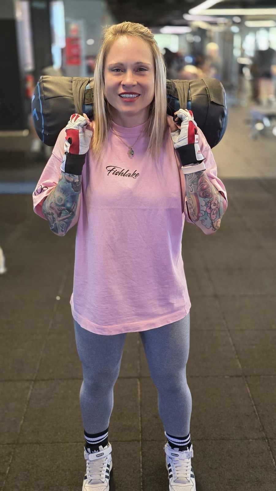 Mujer con camisa rosa y vaqueros sonriendo en el interior de un edificio, haciendo el signo de la paz.