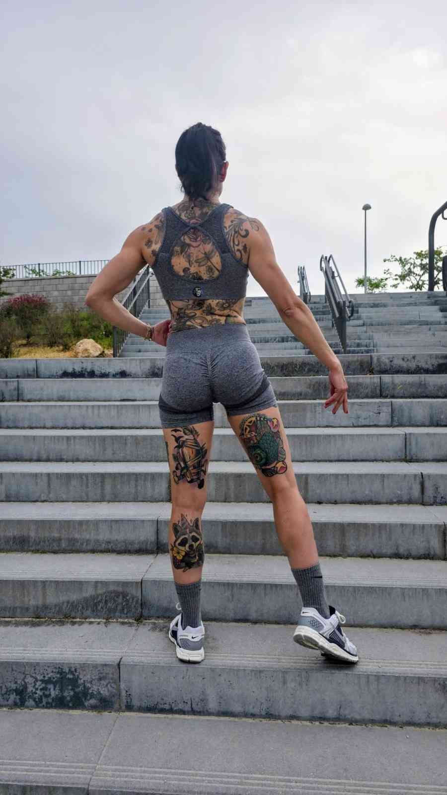 Mujer de pie en unas escaleras exteriores, vista de espaldas, con ropa deportiva estampada de flores y zapatillas deportivas.