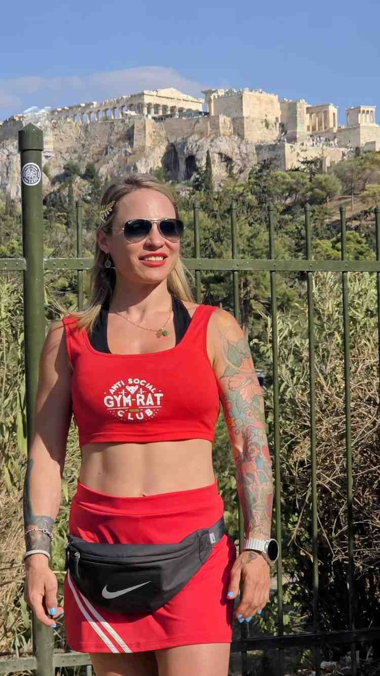 Mujer vestida de rojo y con gafas de sol de pie al aire libre con una histórica fortaleza de piedra al fondo.
