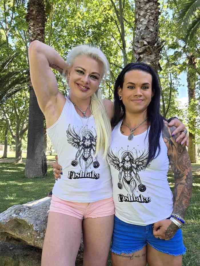Dos mujeres con blusas blancas idénticas posan al aire libre entre palmeras.