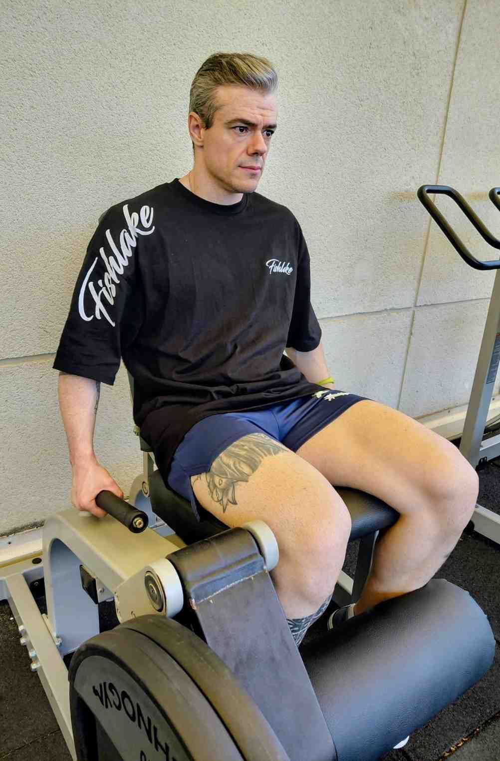 Persona que utiliza una máquina de ejercicios para piernas en un gimnasio, vestida con una camiseta negra.