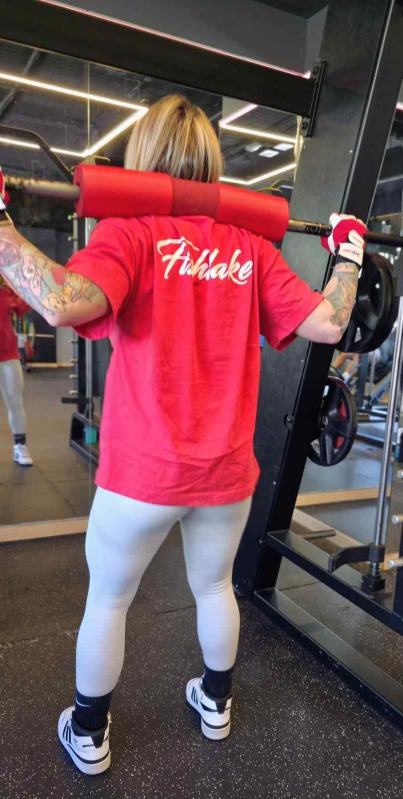 Persona con camiseta roja usando una máquina de pesas en el gimnasio, vista desde atrás.