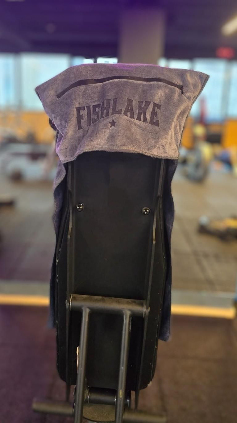 Sudadera gris colgada sobre una silla negra en un interior borroso con equipo de gimnasio al fondo.