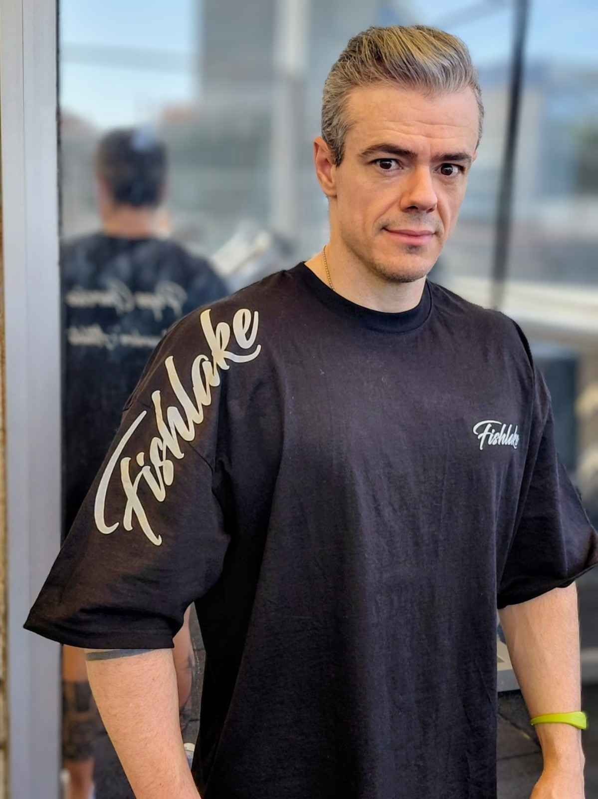 Hombre de pie en el interior de un local, con una camiseta negra con letras grises, mirando a la cámara.