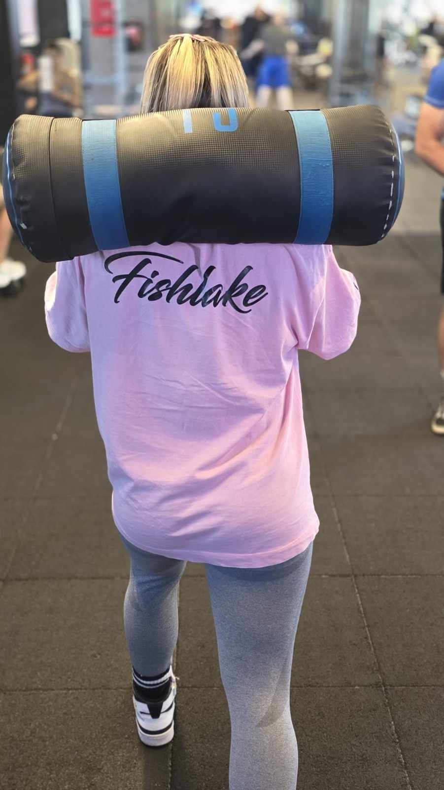 Persona con camisa rosa y vaqueros cargando una colchoneta enrollada grande sobre sus hombros.
